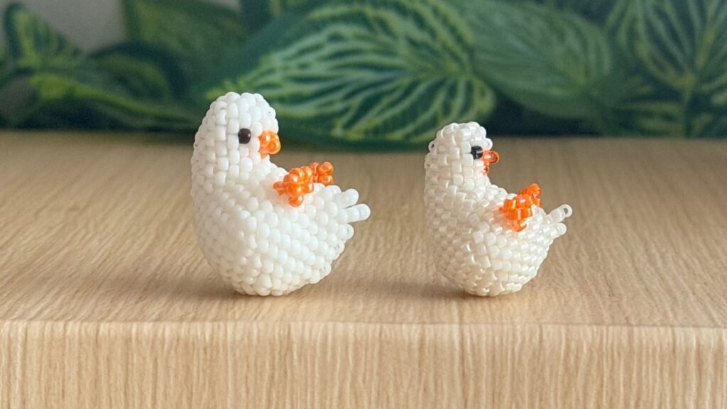 Two white 3D beaded ducks with orange beaks and feet, made with seed beads in circular peyote stitch