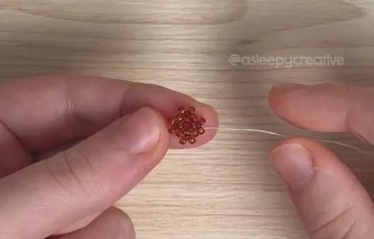 Holding the dark brown peyote stitch cap of a 3D beaded mini acorn after row 3, with the beading thread pulled tight
