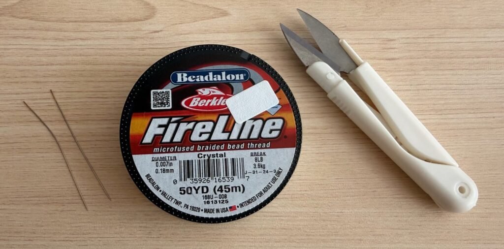 Beading supplies for adding new thread: a spool of Fireline beading thread, two beading needles and thread snips